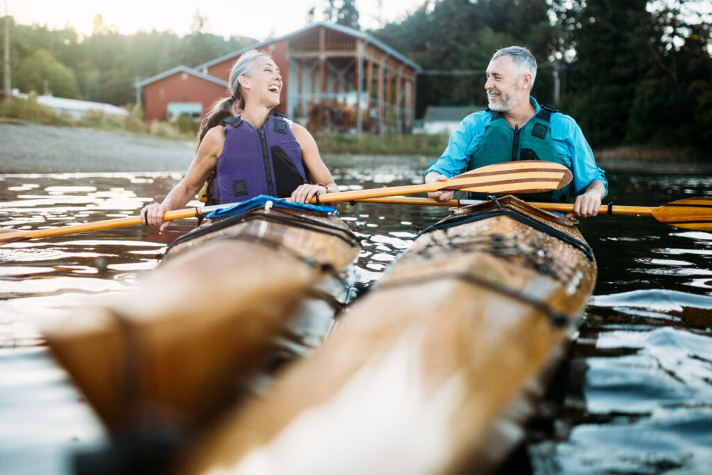 Seniors taking on the world!  A mature couple in their late 50's enjoy paddling their kayaks on a relaxing vacation in Gig Harbor, Washington, the sun shining on the water of the Puget Sound.  A depiction of health and relationship in later years depicting the beauty of aging.