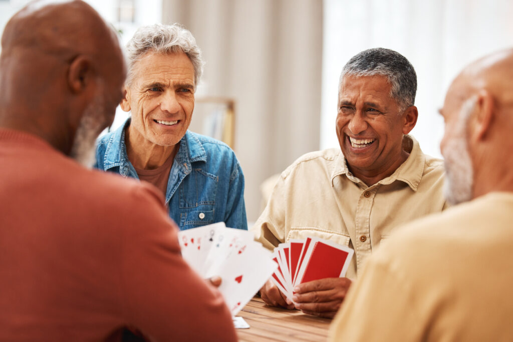 Senior man, friends and laughing for card games on wooden table in fun activity, social bonding or gathering. Group of happy elderly men with cards for poker game enjoying play time together at home